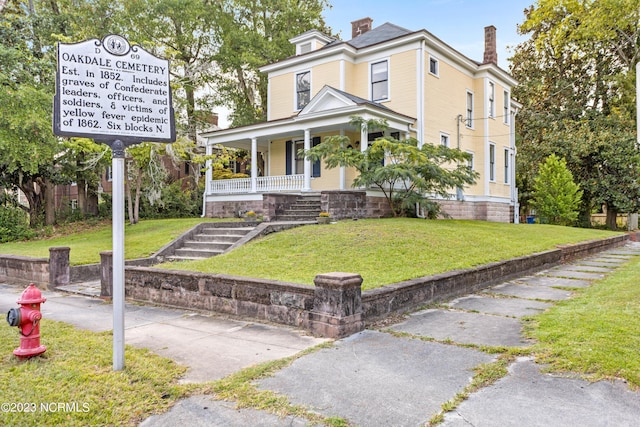 view of front facade with covered porch, a chimney, and a front yard