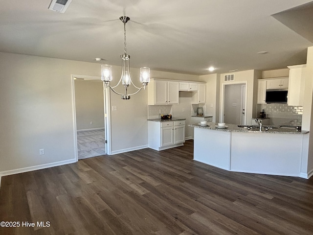 kitchen with hanging light fixtures, white cabinets, dark wood-type flooring, and light stone counters