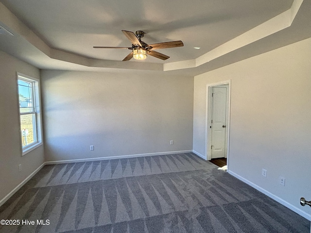 empty room featuring ceiling fan, dark carpet, and a tray ceiling