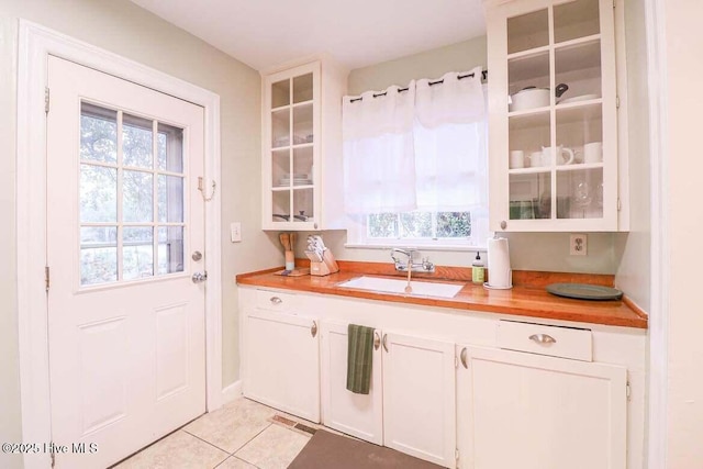 kitchen featuring light tile patterned floors, sink, white cabinets, and wooden counters