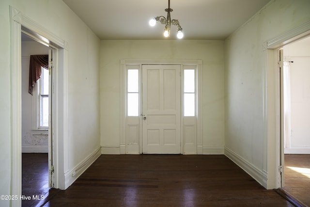 entryway with dark wood-type flooring, a wealth of natural light, and a notable chandelier