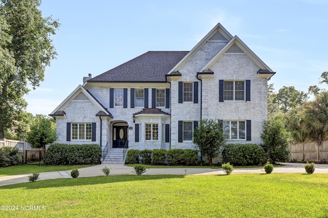 view of front of property featuring brick siding, a chimney, a front yard, and fence