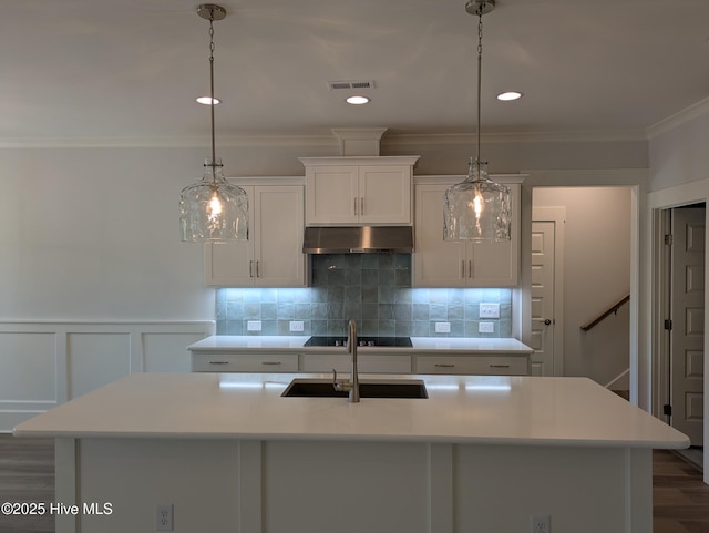 kitchen featuring an island with sink, ornamental molding, light countertops, under cabinet range hood, and backsplash