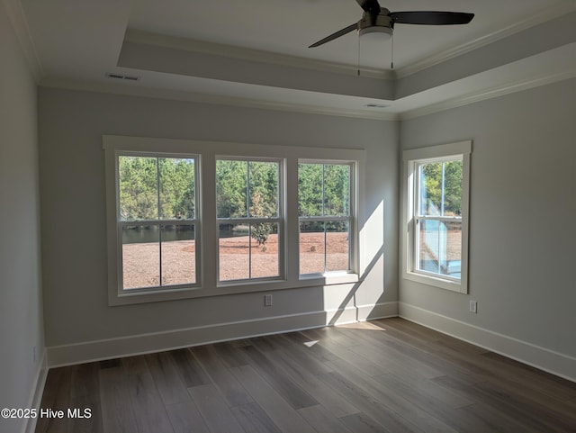 empty room with dark wood-style floors, visible vents, a tray ceiling, and ornamental molding