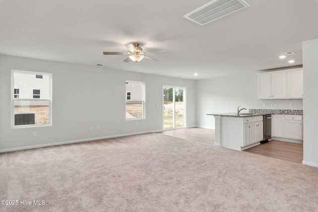 unfurnished living room with ceiling fan, light colored carpet, and sink