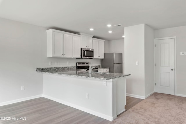 kitchen featuring white cabinetry, kitchen peninsula, stainless steel appliances, light stone counters, and sink