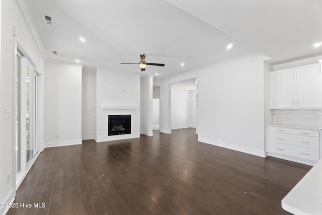 unfurnished living room featuring ceiling fan, a large fireplace, dark hardwood / wood-style flooring, and crown molding