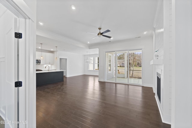 unfurnished living room with crown molding, dark hardwood / wood-style flooring, sink, and ceiling fan with notable chandelier