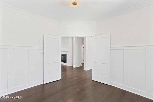 spare room featuring a brick fireplace, dark hardwood / wood-style flooring, and ornamental molding