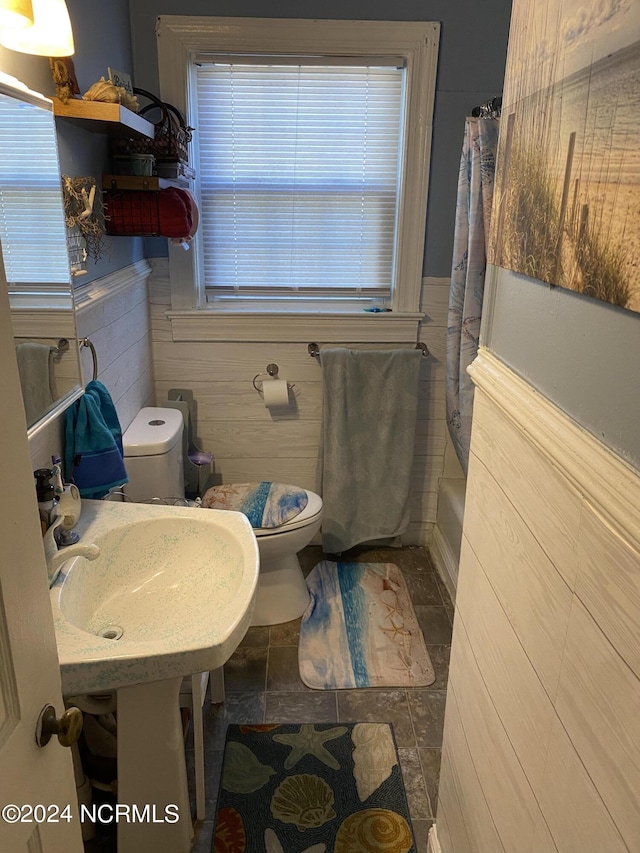 full bathroom with sink, toilet, wood walls, and shower / tub combo with curtain