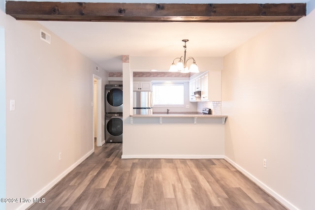 kitchen featuring decorative light fixtures, kitchen peninsula, stainless steel refrigerator, white cabinetry, and stacked washer and clothes dryer