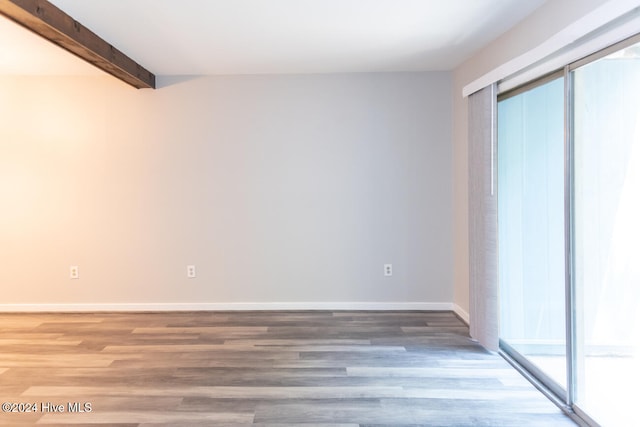 spare room featuring a healthy amount of sunlight, beam ceiling, and hardwood / wood-style flooring