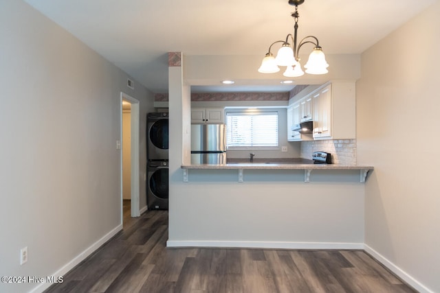 kitchen with stacked washer / dryer, decorative light fixtures, white cabinetry, kitchen peninsula, and stainless steel refrigerator