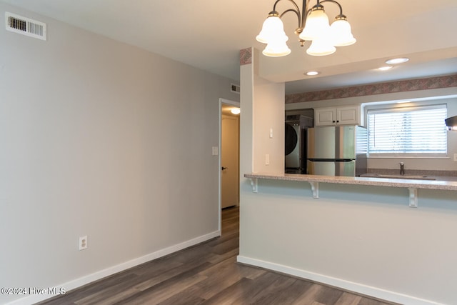 kitchen with hanging light fixtures, stainless steel refrigerator, stacked washing maching and dryer, a chandelier, and a breakfast bar