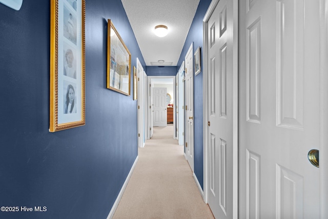 hallway featuring light colored carpet and a textured ceiling