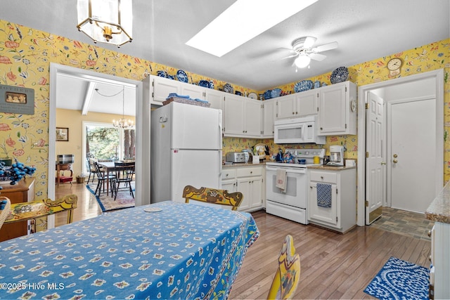 kitchen with a skylight, white cabinetry, white appliances, ceiling fan with notable chandelier, and light hardwood / wood-style flooring