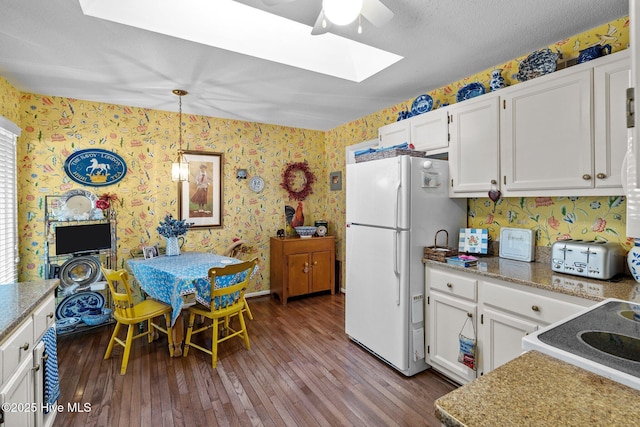 kitchen featuring white fridge, a skylight, white cabinetry, hardwood / wood-style floors, and pendant lighting