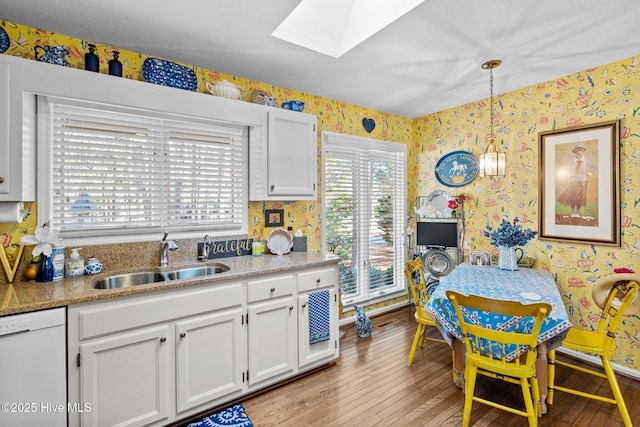 kitchen with decorative light fixtures, dishwasher, sink, and white cabinetry