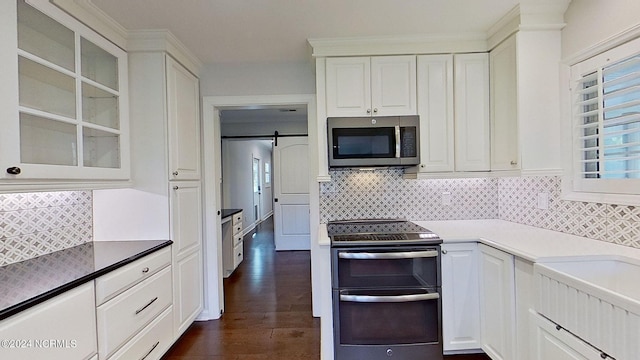 kitchen featuring a barn door, backsplash, dark hardwood / wood-style floors, white cabinetry, and stainless steel appliances