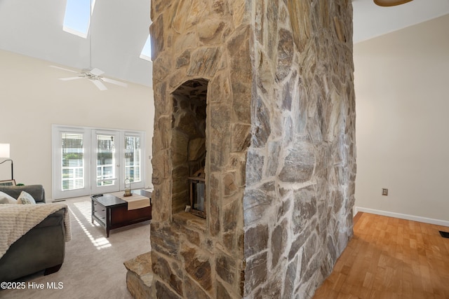 living room featuring ceiling fan, hardwood / wood-style floors, a skylight, a stone fireplace, and high vaulted ceiling