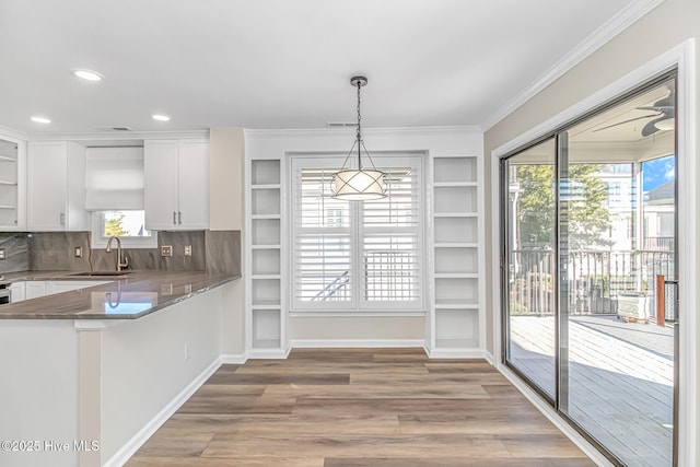 kitchen with kitchen peninsula, tasteful backsplash, pendant lighting, white cabinets, and sink