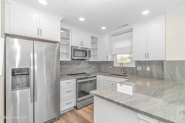 kitchen with white cabinetry, stainless steel appliances, sink, kitchen peninsula, and light stone counters