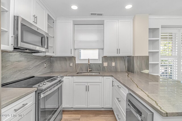 kitchen with white cabinetry, stainless steel appliances, sink, kitchen peninsula, and light stone counters