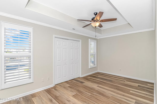 unfurnished bedroom with ceiling fan, a tray ceiling, a closet, ornamental molding, and light hardwood / wood-style flooring