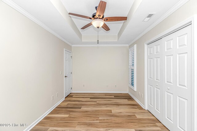unfurnished bedroom with ceiling fan, a tray ceiling, a closet, ornamental molding, and light hardwood / wood-style flooring