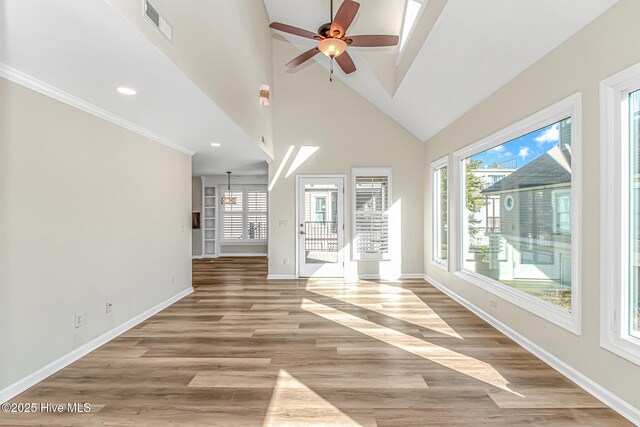 unfurnished living room featuring ceiling fan, vaulted ceiling with skylight, crown molding, and light wood-type flooring