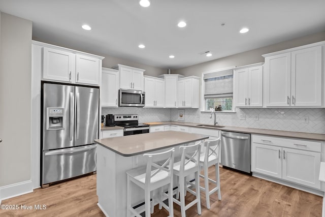 kitchen featuring stainless steel appliances, a center island, sink, and white cabinets