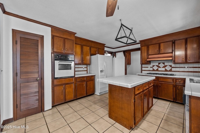 kitchen with tile countertops, appliances with stainless steel finishes, decorative backsplash, a kitchen island, and crown molding