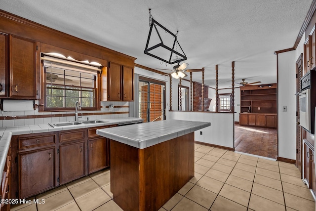 kitchen featuring a center island, tile counters, sink, hanging light fixtures, and crown molding