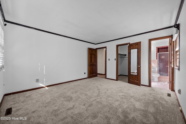 unfurnished bedroom with a spacious closet, light carpet, ensuite bath, a closet, and ornamental molding