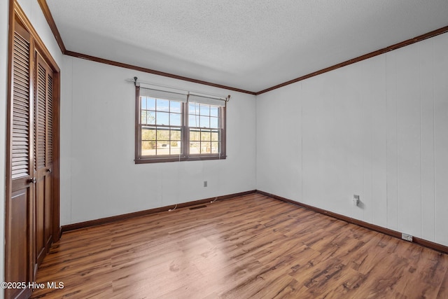 unfurnished bedroom with crown molding, light wood-type flooring, a closet, and a textured ceiling