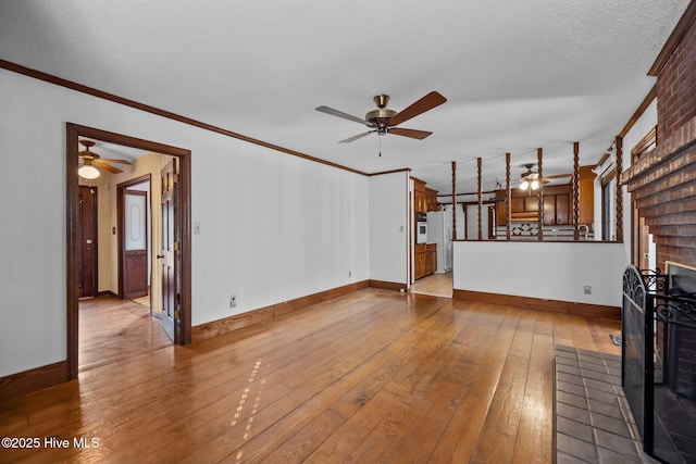 unfurnished living room featuring ceiling fan, a fireplace, crown molding, light hardwood / wood-style flooring, and a textured ceiling