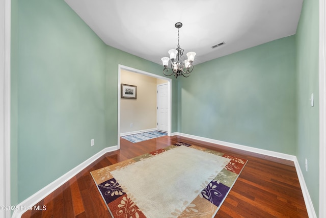 unfurnished room featuring dark wood-type flooring and a notable chandelier