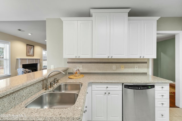 kitchen featuring tasteful backsplash, sink, white cabinets, stainless steel dishwasher, and light stone counters