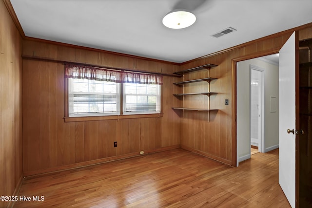 empty room with light wood-type flooring, crown molding, and wooden walls