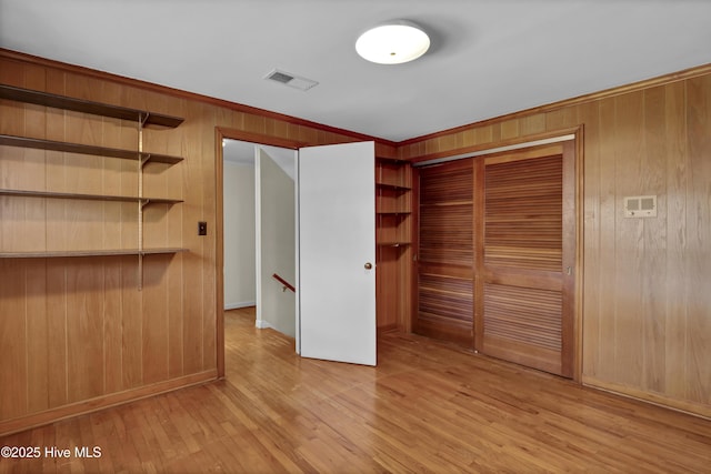 unfurnished bedroom with light wood-type flooring, a closet, crown molding, and wooden walls