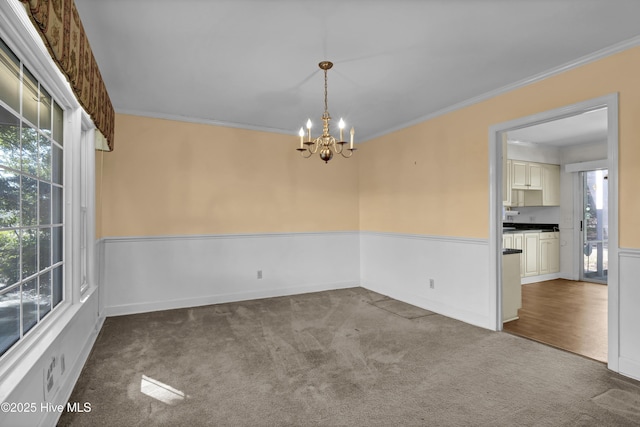 carpeted empty room featuring a wealth of natural light, an inviting chandelier, and ornamental molding