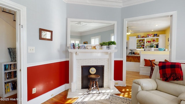 sitting room with a fireplace, wood finished floors, crown molding, and ceiling fan