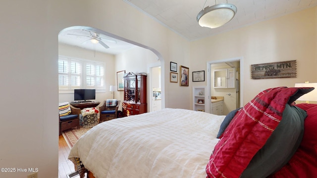 bedroom with arched walkways, ornamental molding, wood finished floors, and ensuite bathroom