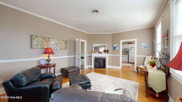 living area with a premium fireplace, light wood-type flooring, visible vents, and ornamental molding