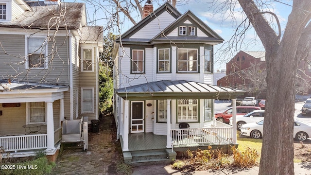 victorian home featuring a chimney, a standing seam roof, metal roof, and covered porch