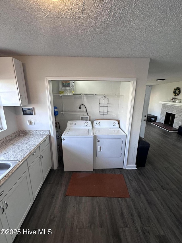 laundry area with dark wood-type flooring, a fireplace with raised hearth, washer and dryer, a textured ceiling, and laundry area