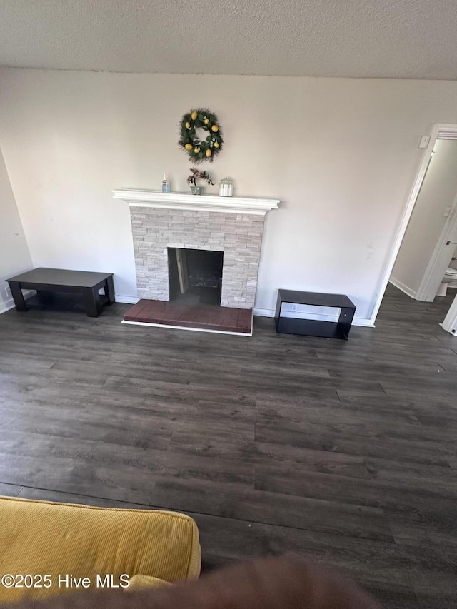 living room with dark wood-type flooring, a fireplace with raised hearth, baseboards, and a textured ceiling