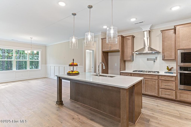 kitchen featuring pendant lighting, sink, wall chimney range hood, and a kitchen island with sink