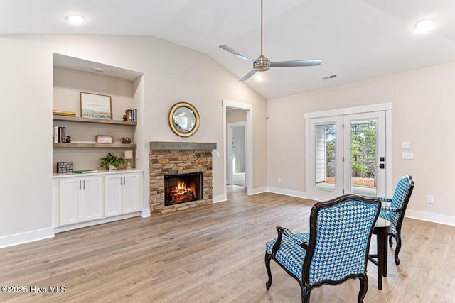 living room featuring a stone fireplace, lofted ceiling, ceiling fan, light hardwood / wood-style floors, and built in shelves