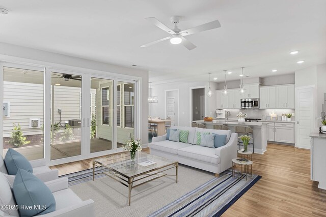 living room featuring ceiling fan, sink, and light wood-type flooring